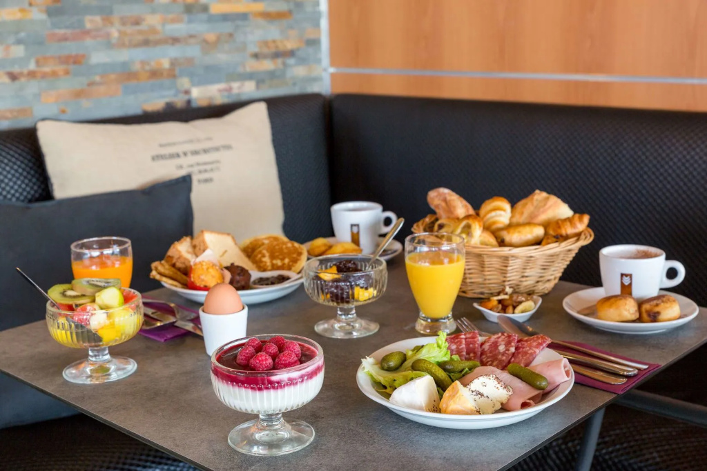 Table de petit-déjeuner avec viennoiseries, fruits frais, charcuterie, fromage, jus d'orange et café
